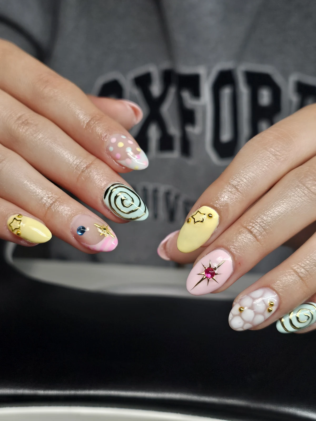 Pastel almond nails with gold spirals, star charms, colourful gems and dotted accents.