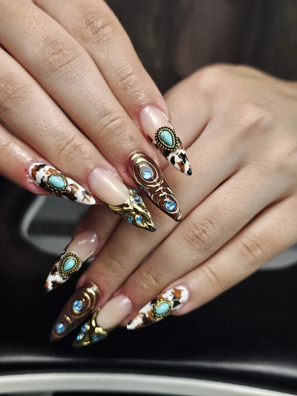 Long pointed nails with cow-print tips, turquoise-coloured stones, gold spirals and blue gems.