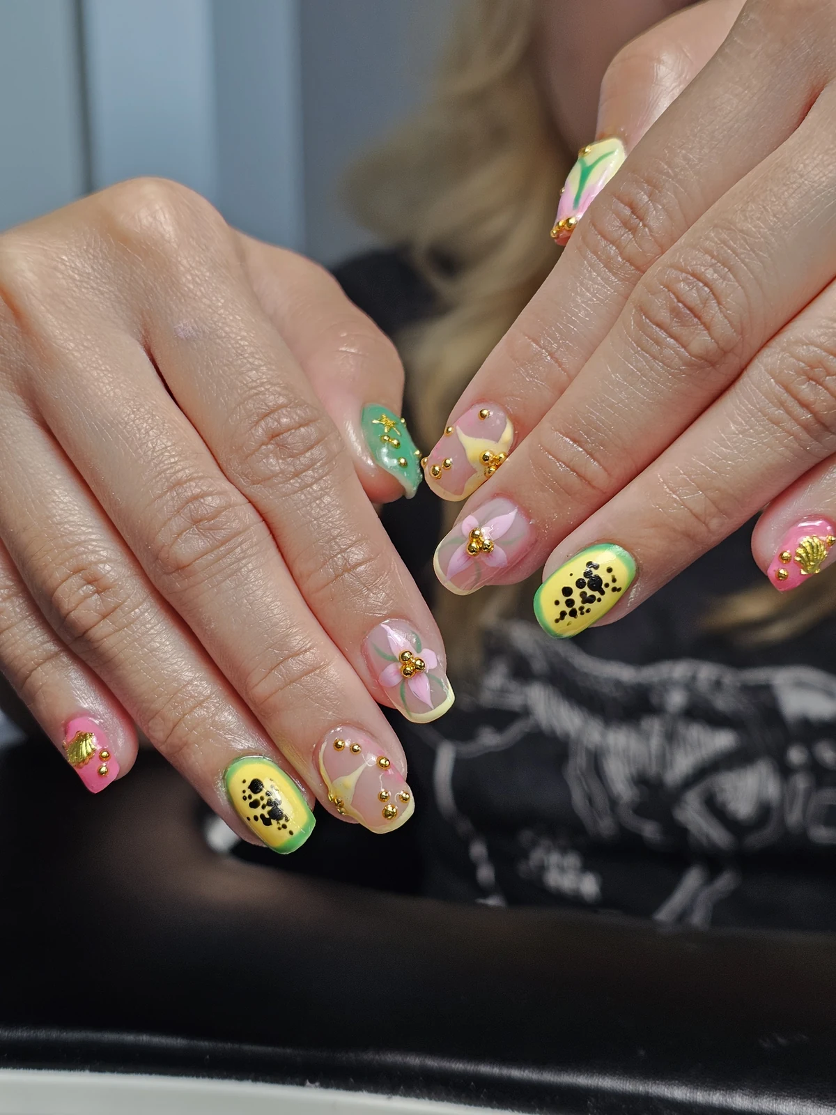 Pink, green and yellow nails with floral and fruit-inspired art, gold beads and shell charms.