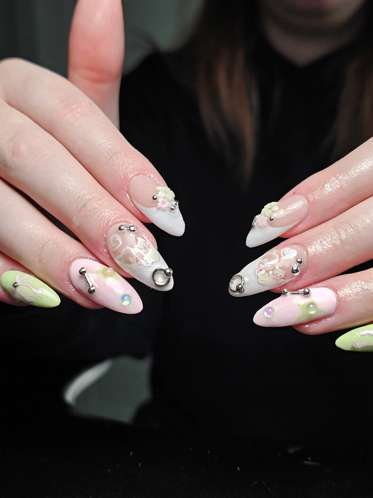 Pastel pink, green and white almond nails with flowers, heart details and silver rings and bars.
