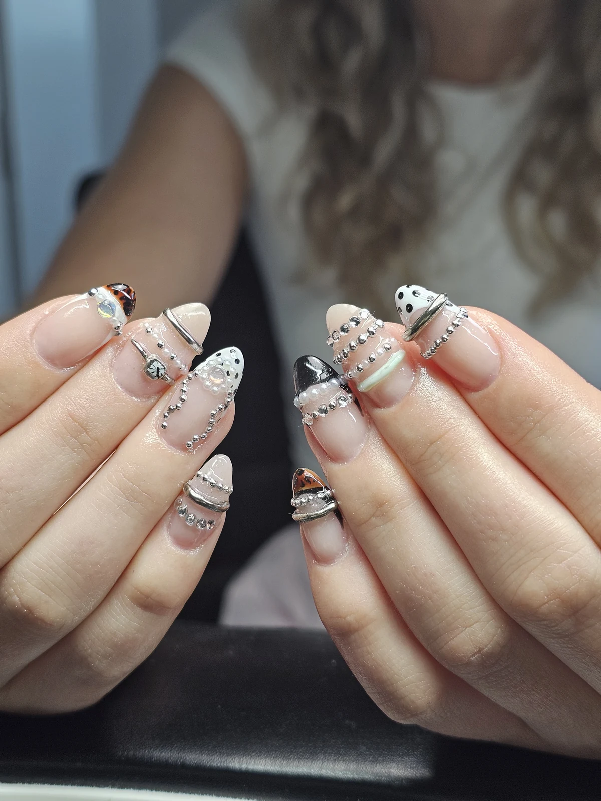 Nude almond nails with patterned tips, silver bands and beads, crystals and pearl accents.
