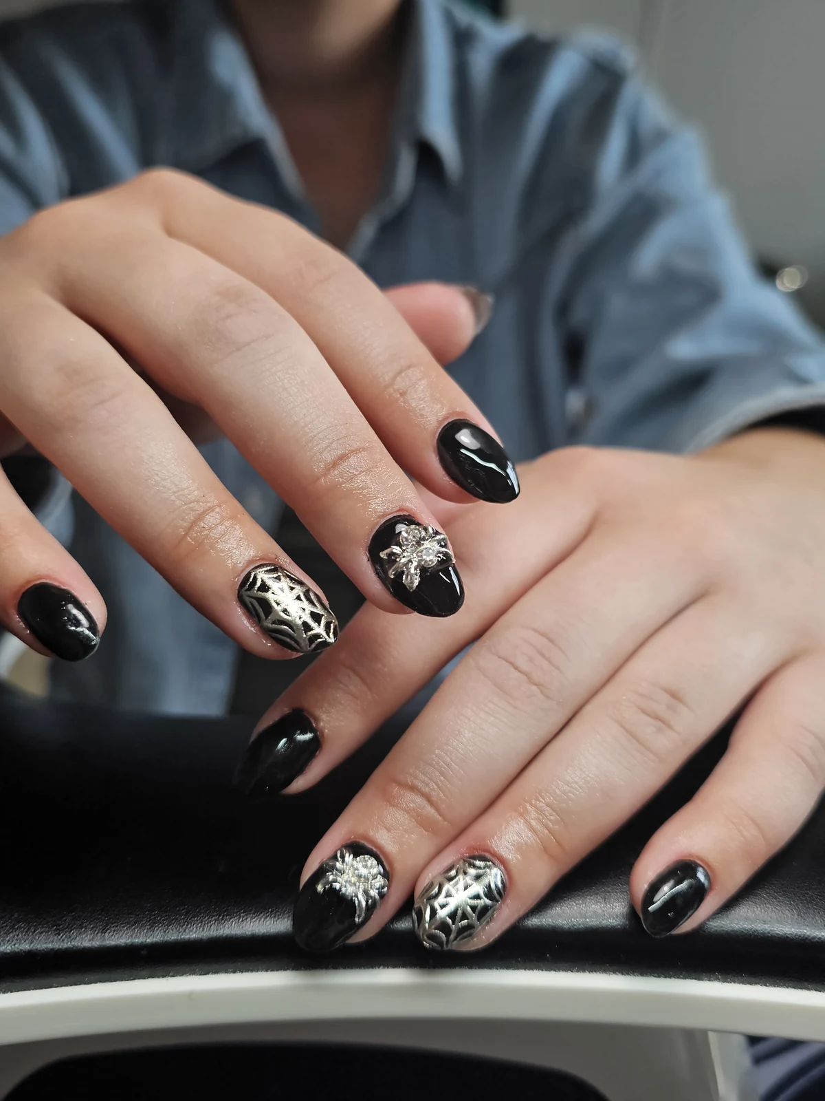 Glossy black nails with silver spiderweb patterns and jewelled spider charms.