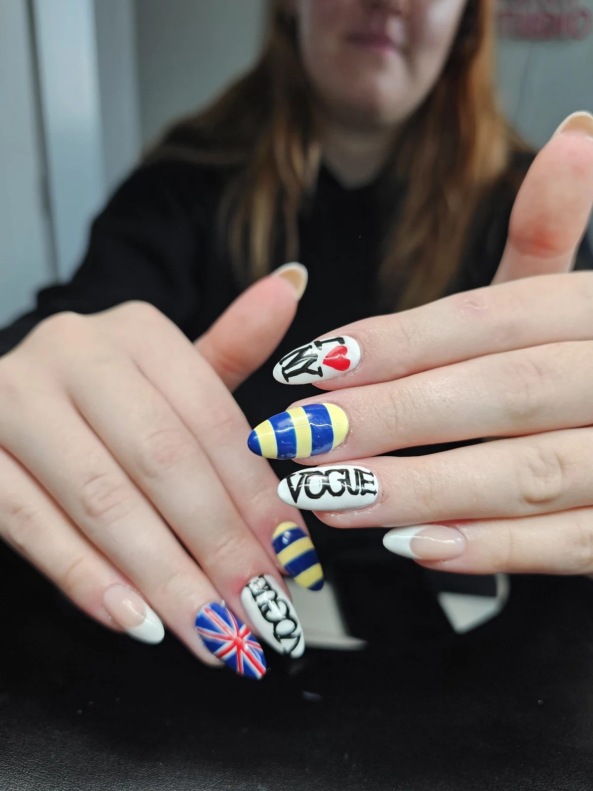 Almond nails with white French tips, blue and yellow stripes, a Union Jack and black lettering.