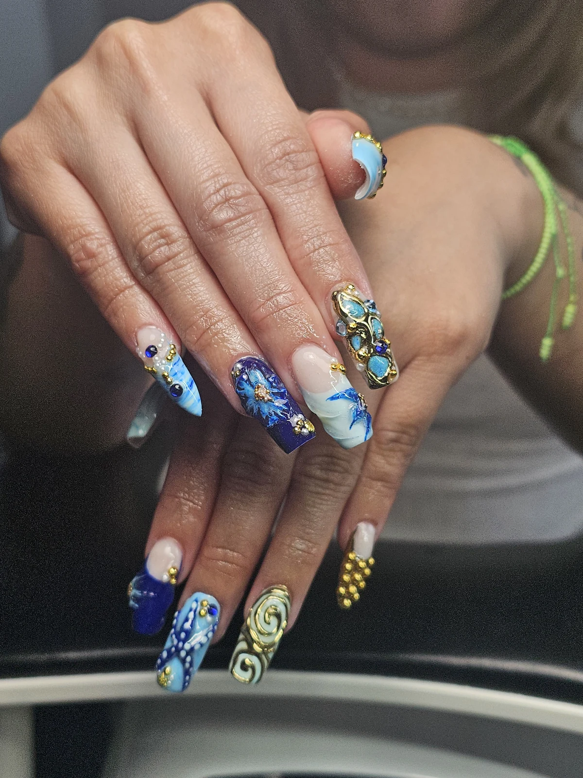 Long blue and mint nails with flowers, gold spirals, blue stones and pearl accents.