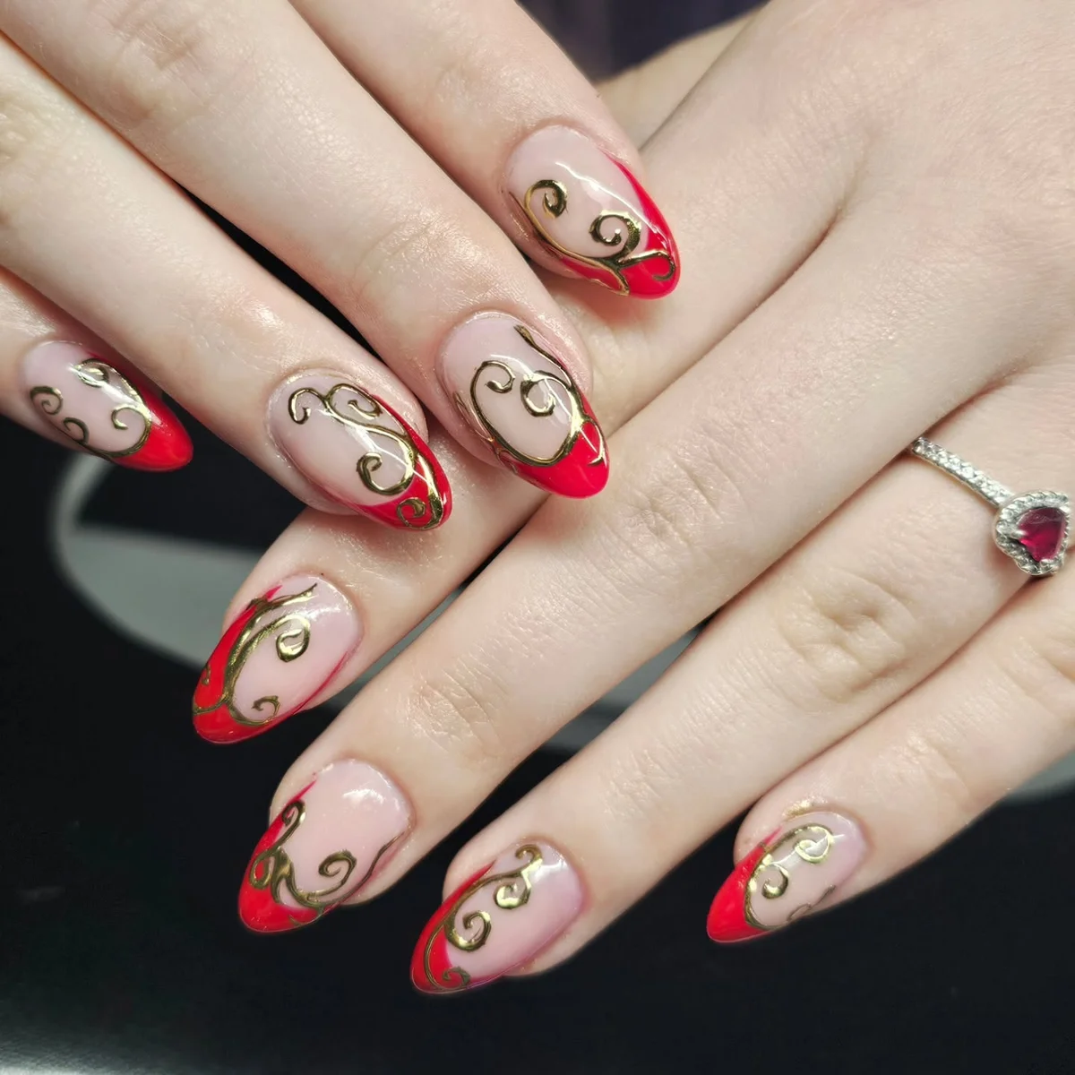 Nude nails with red French tips and gold swirl details