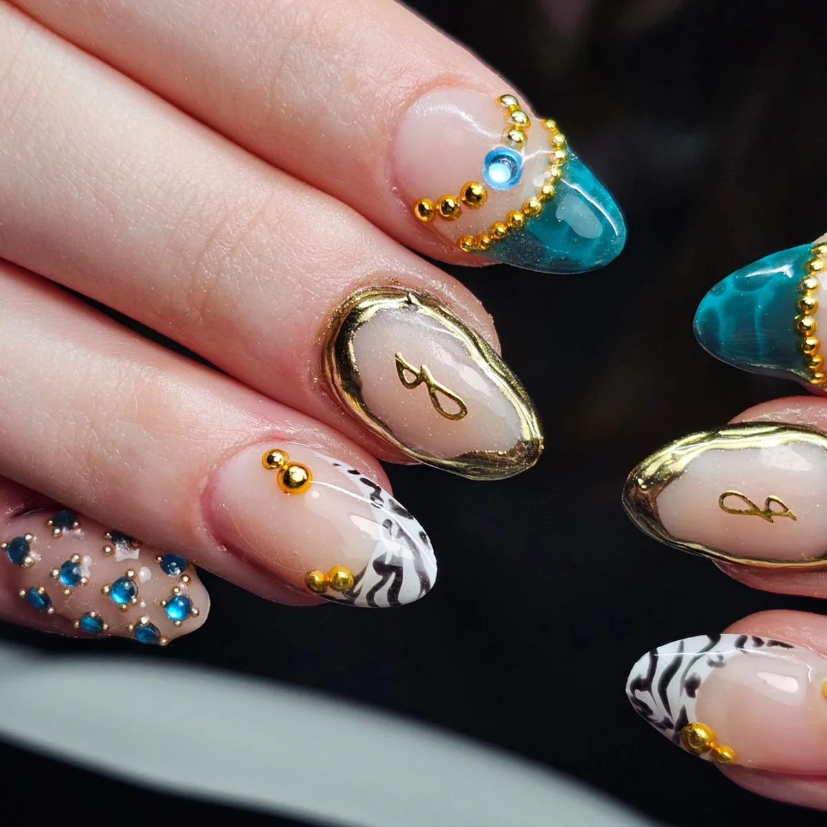 Nude nails with blue and gold accents and contrasting patterned tips