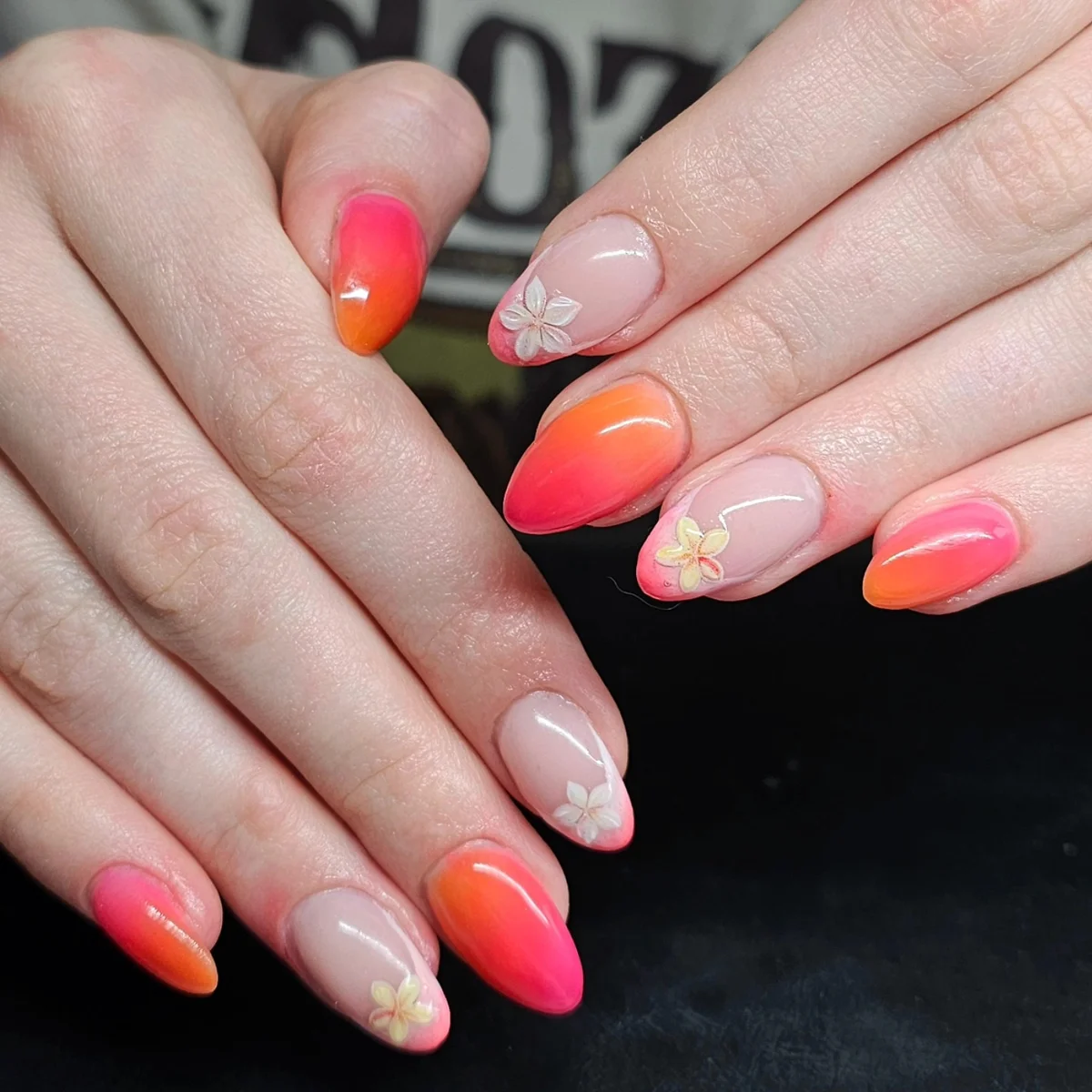 Nude nails with bright pink-to-orange tips and white flowers