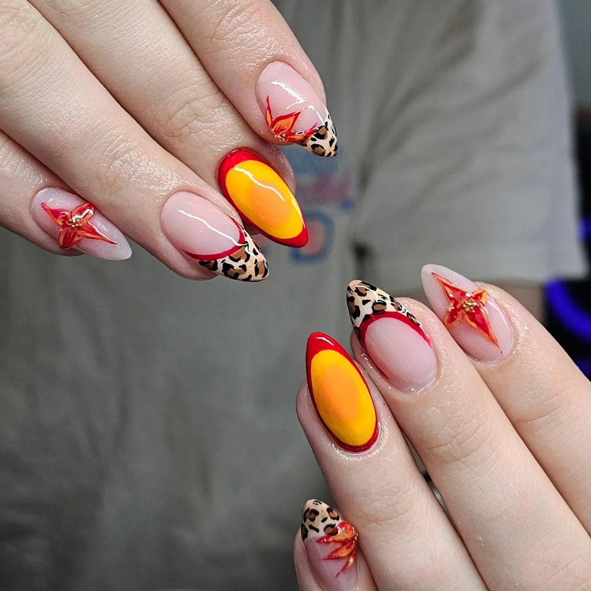 Nude nails with leopard-print tips, red star accents and bright yellow centres.