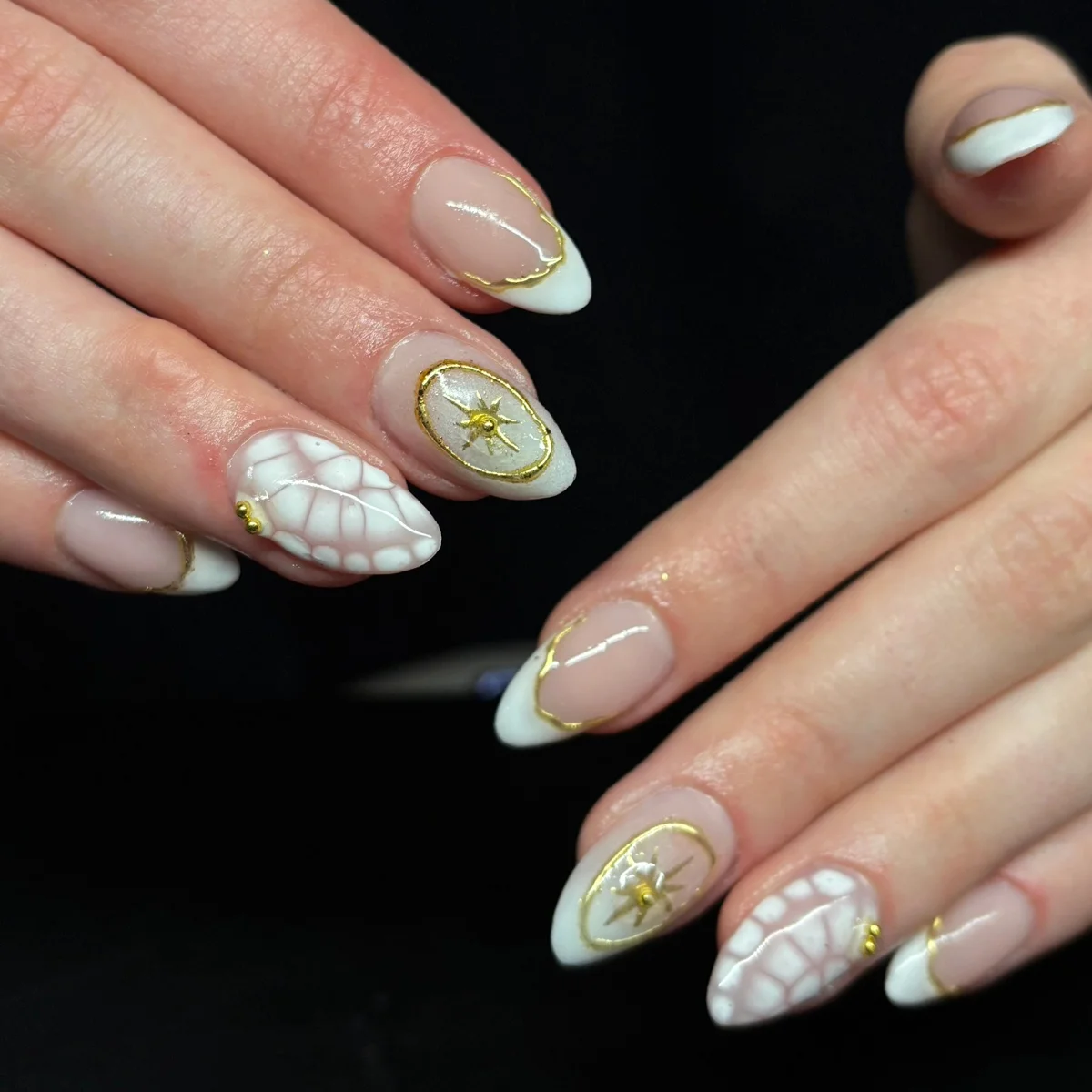 Nude almond nails with white tips, white bubble patterns and gold star details.