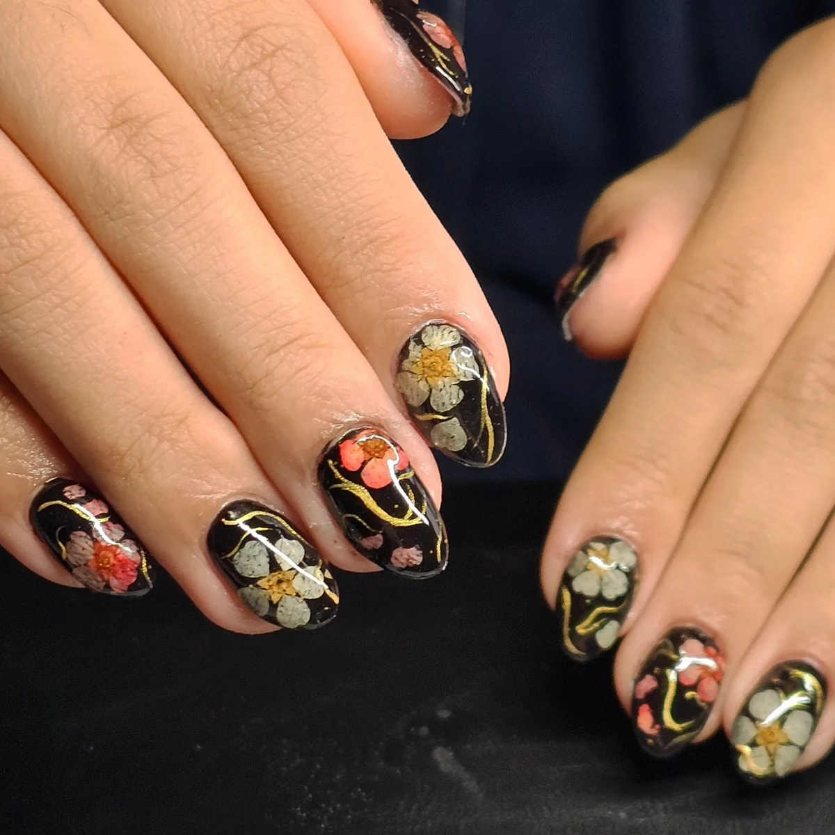 Black nails with colourful flowers and fine gold curved lines.