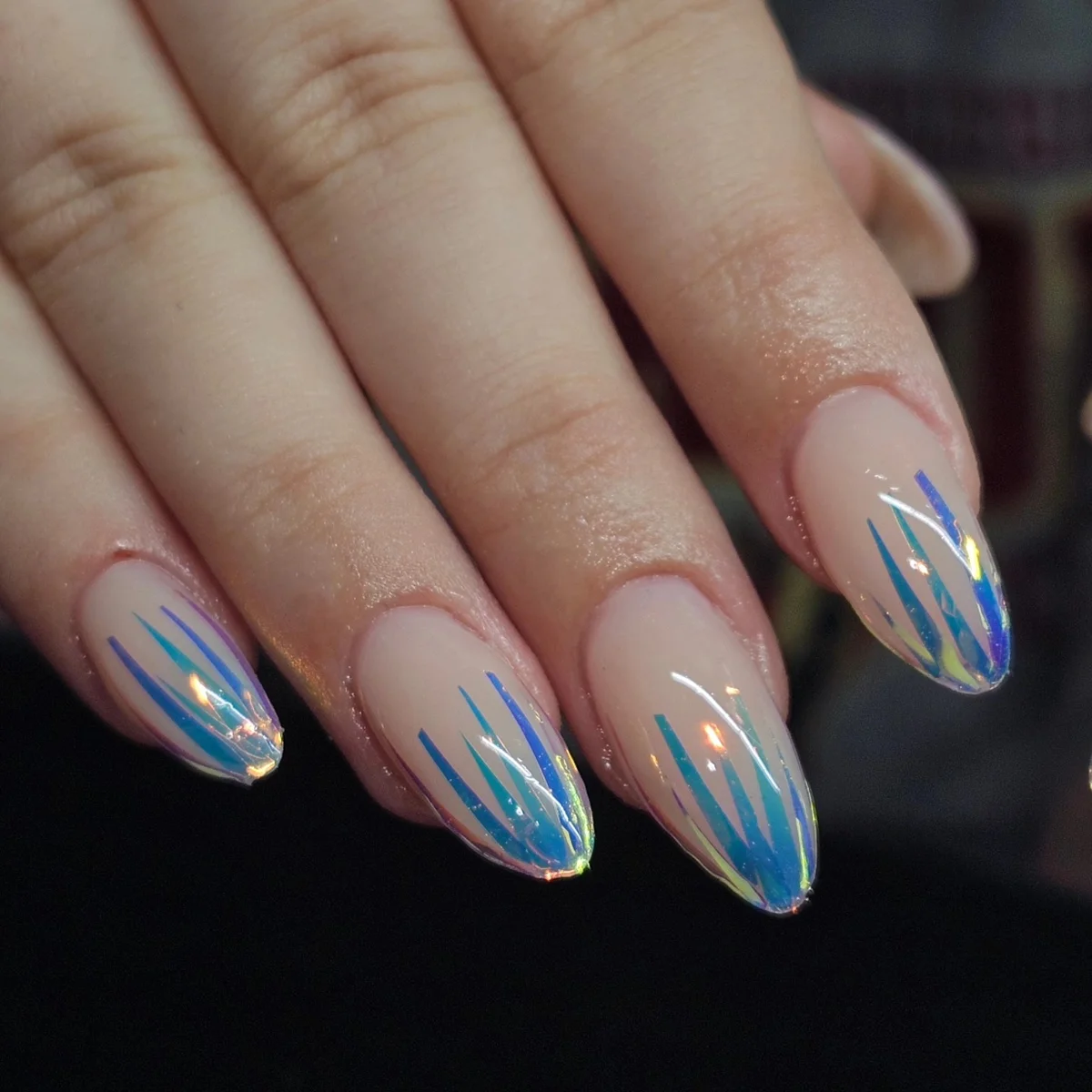 Nude almond nails with blue and iridescent streaks at the tips.