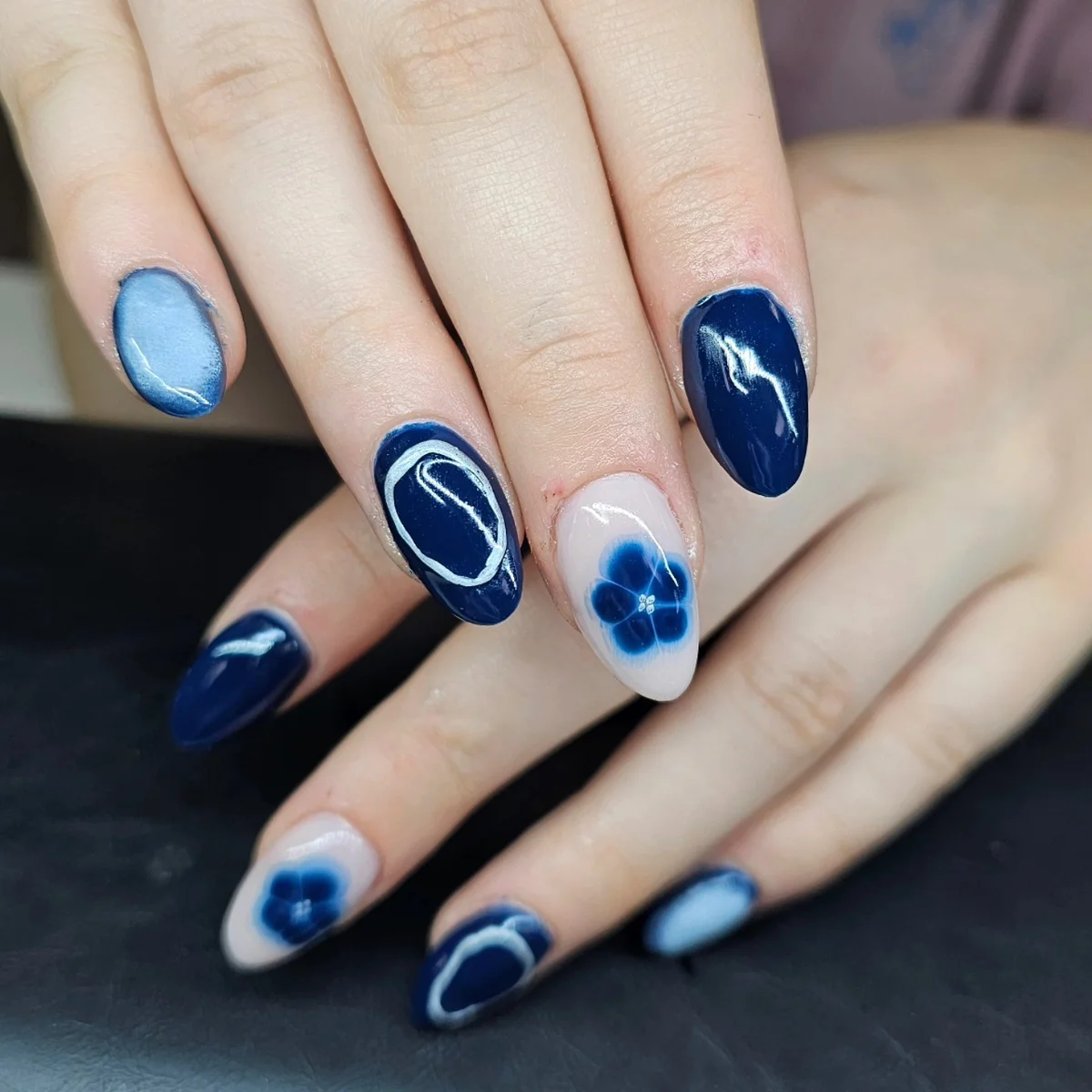 Navy and light blue almond nails with blue flowers and pale curved outlines.