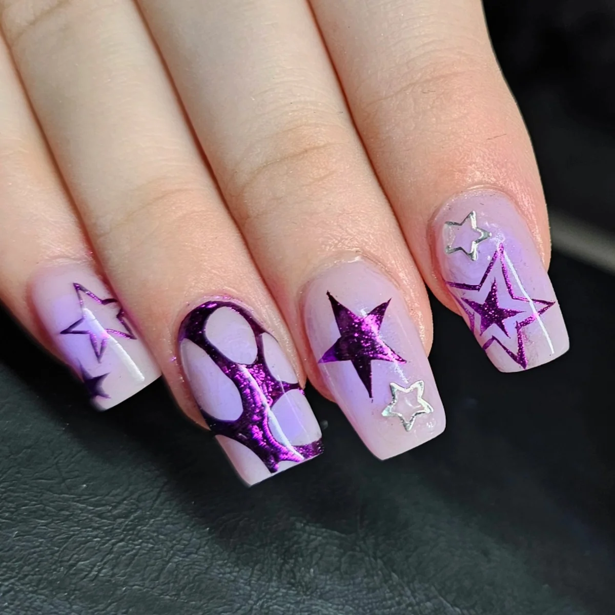Square lilac nails with purple stars and bold curved patterns.