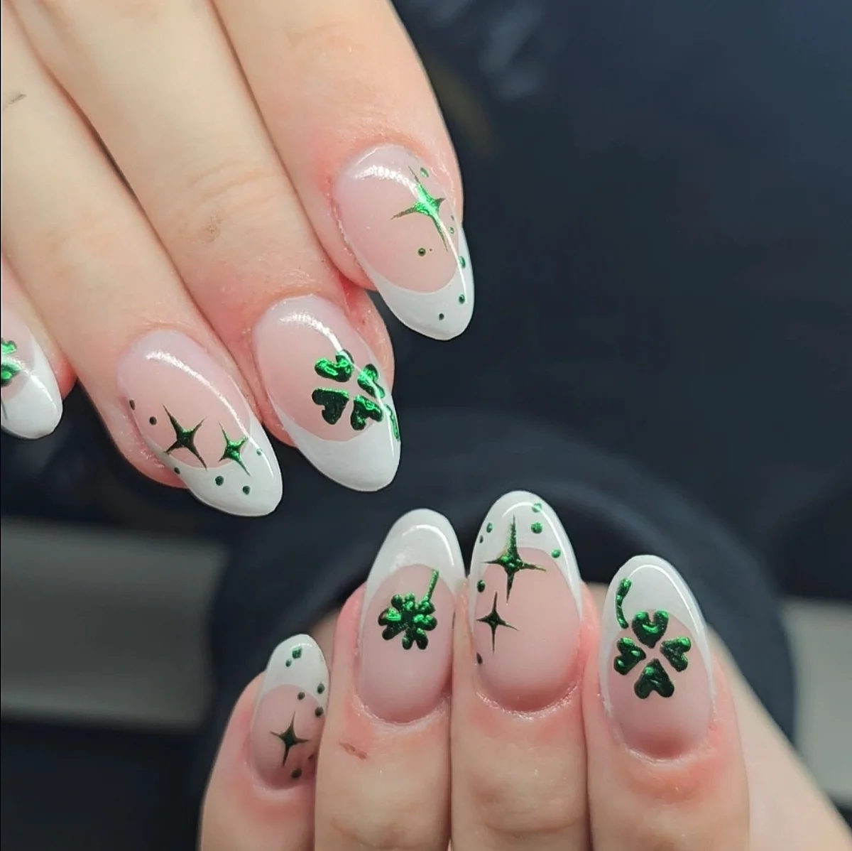 Nude almond nails with pale tips, green flowers and green star accents.