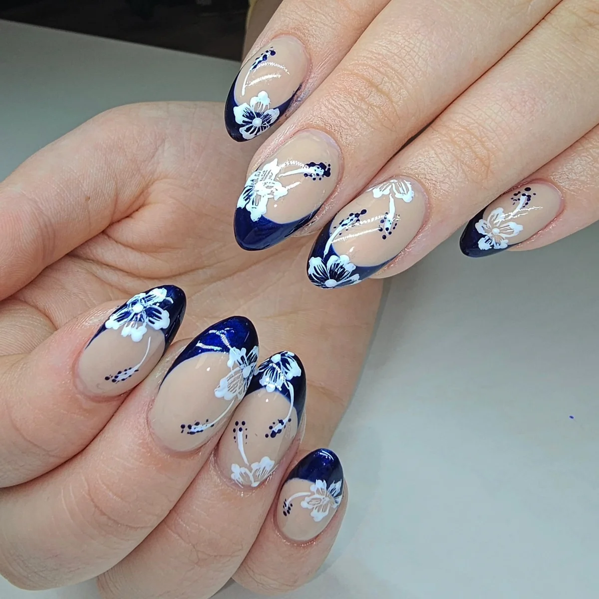 Nude almond nails with navy tips, blue flowers and silver details.