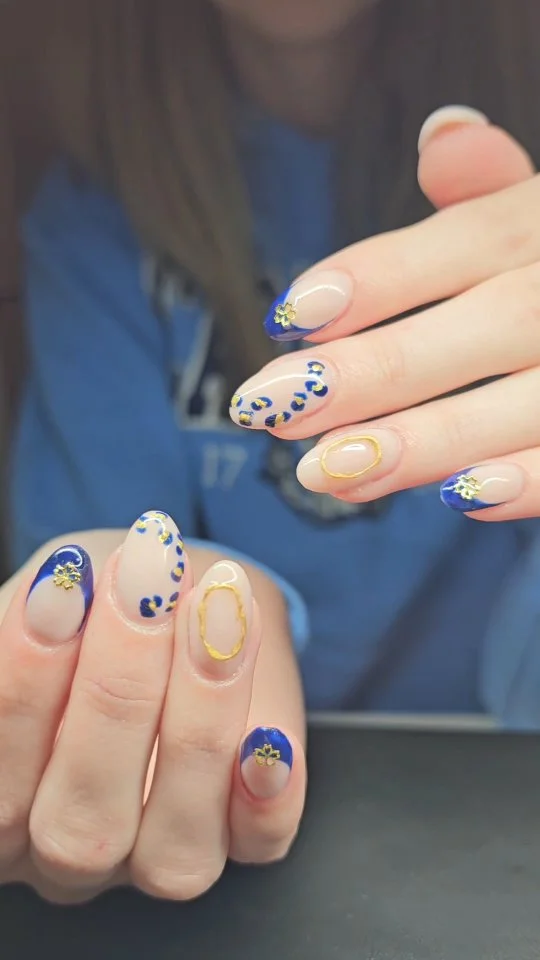 Nude almond nails with blue patterns and thin yellow outlines.