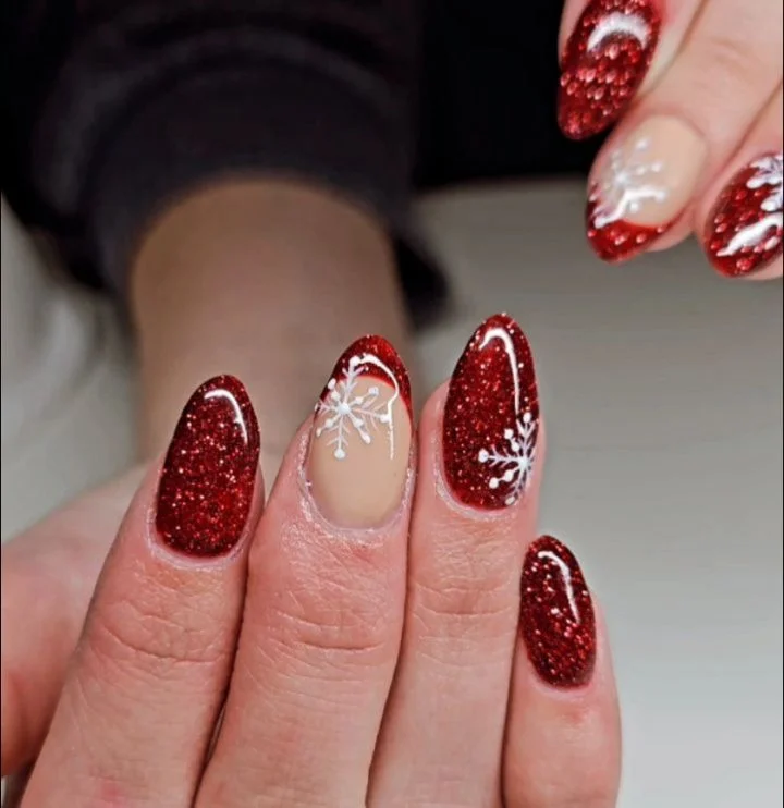 Red glitter and nude nails with white snowflake details.
