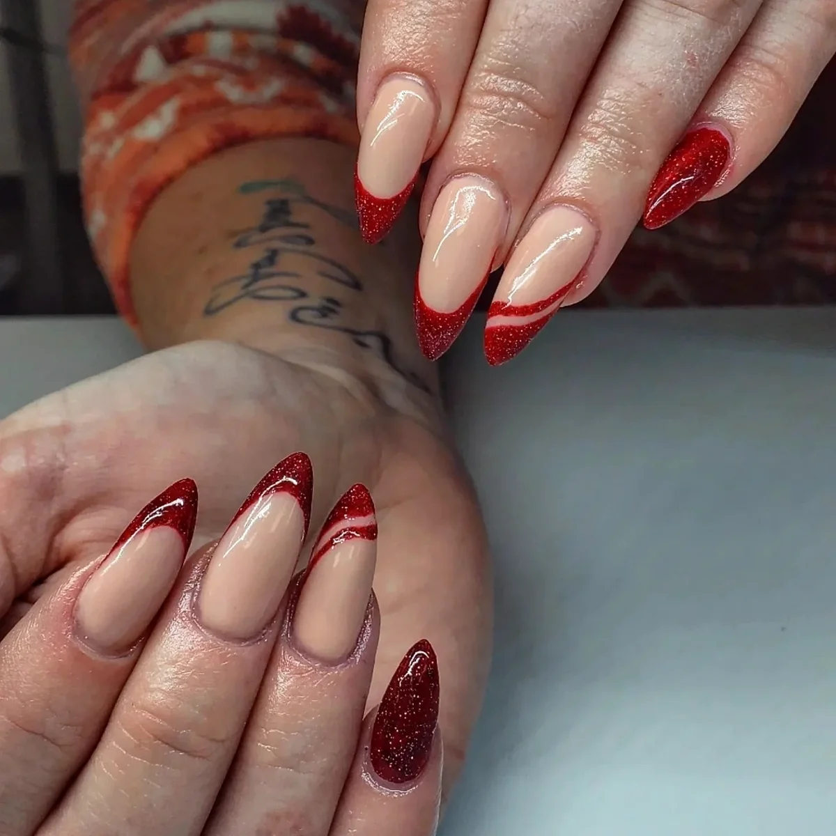 Nude almond nails with red glitter French tips and thin red accents.