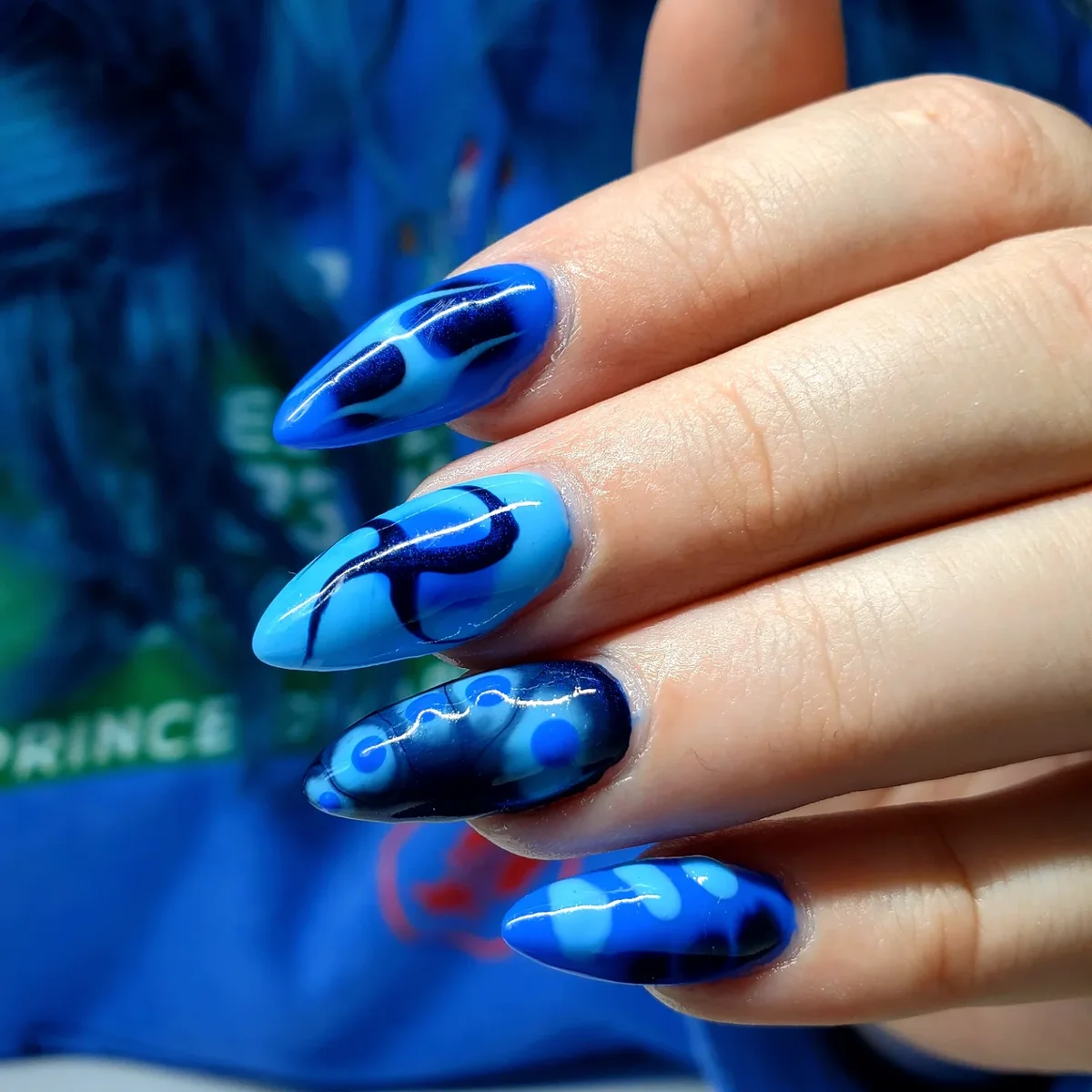 Long blue nails with dark blue curved shapes and pale bubble-like patterns.