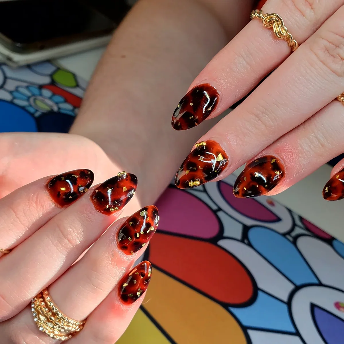 Orange and black almond nails with mottled patterns and gold accents.
