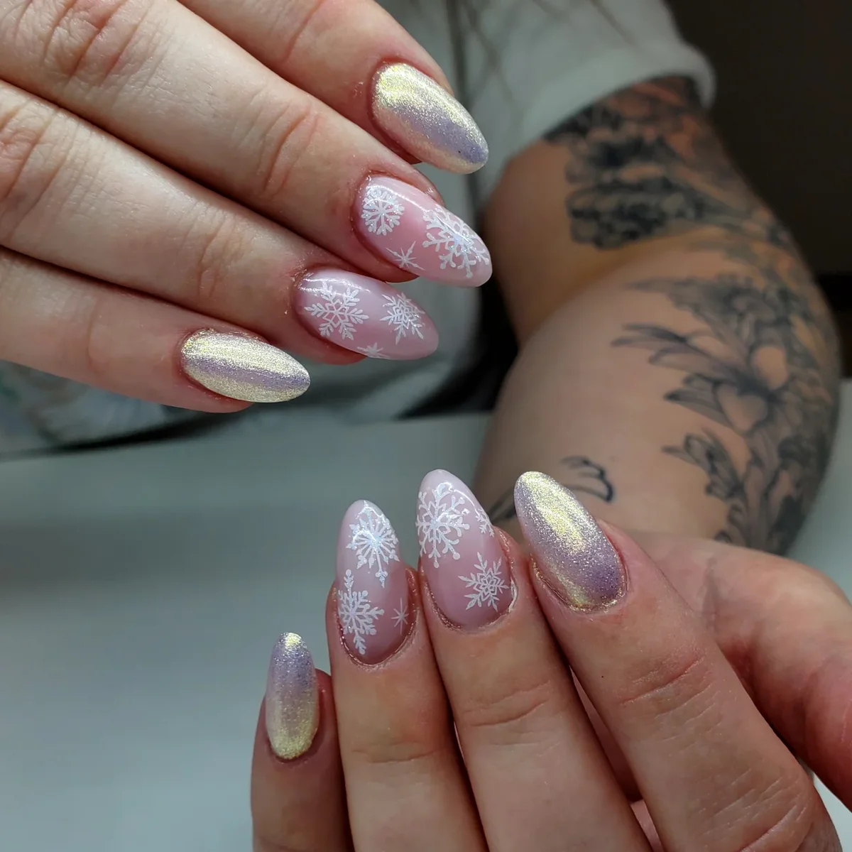 Pink and shimmering pale nails with white snowflake accents.