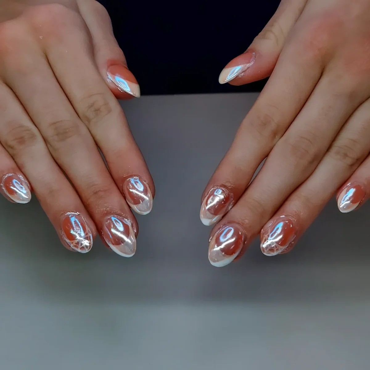 Nude almond nails with orange tips and reflective silver curved details.