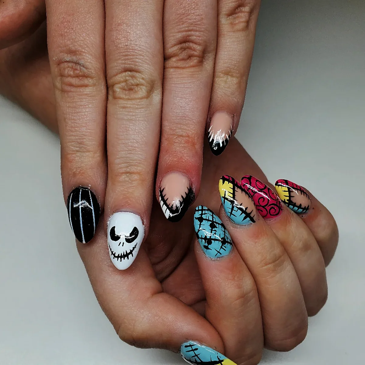 Black, white, pink and blue nails with skull faces, stitched patterns and pointed accents.