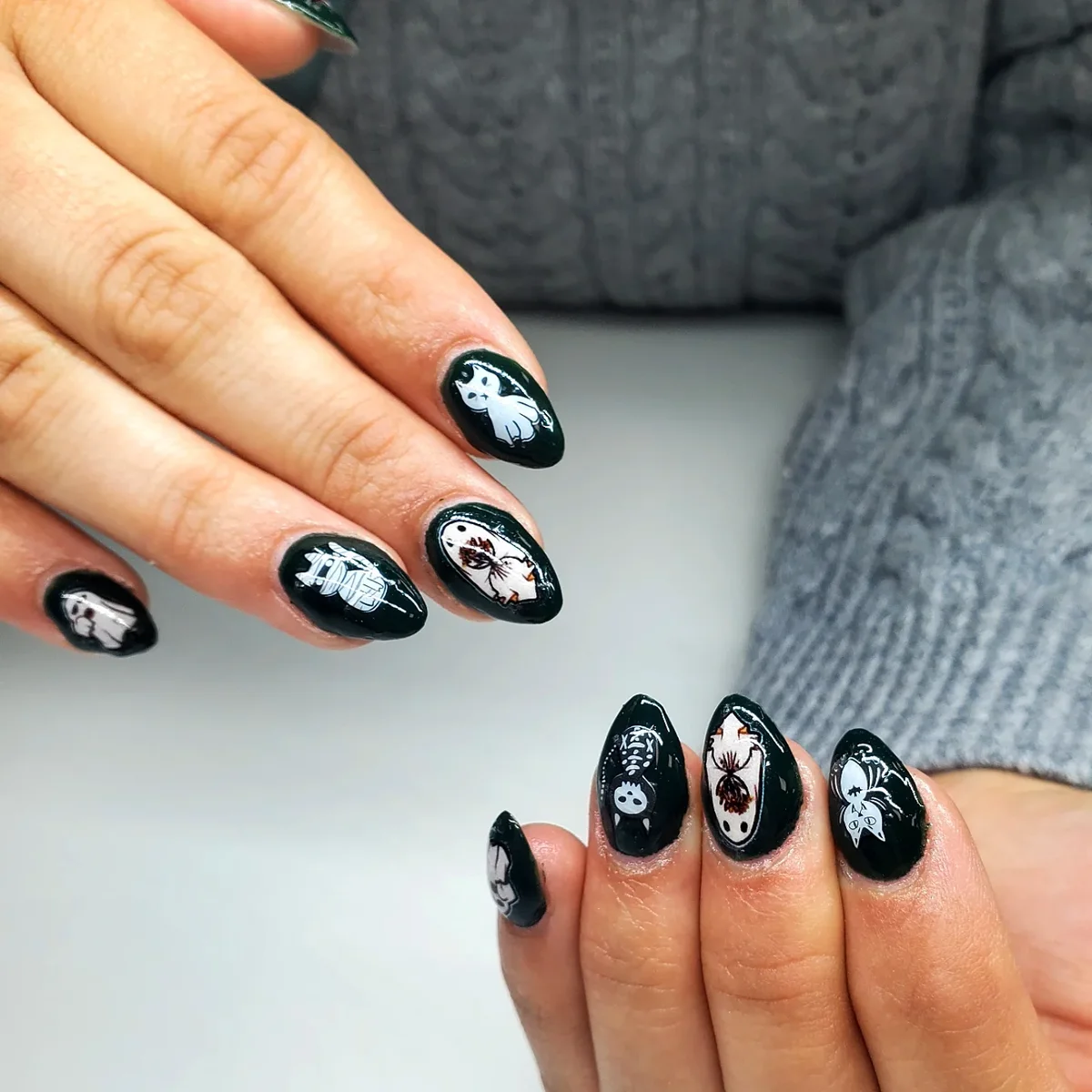Black almond nails with white skeletal figures, faces and small dotted accents.