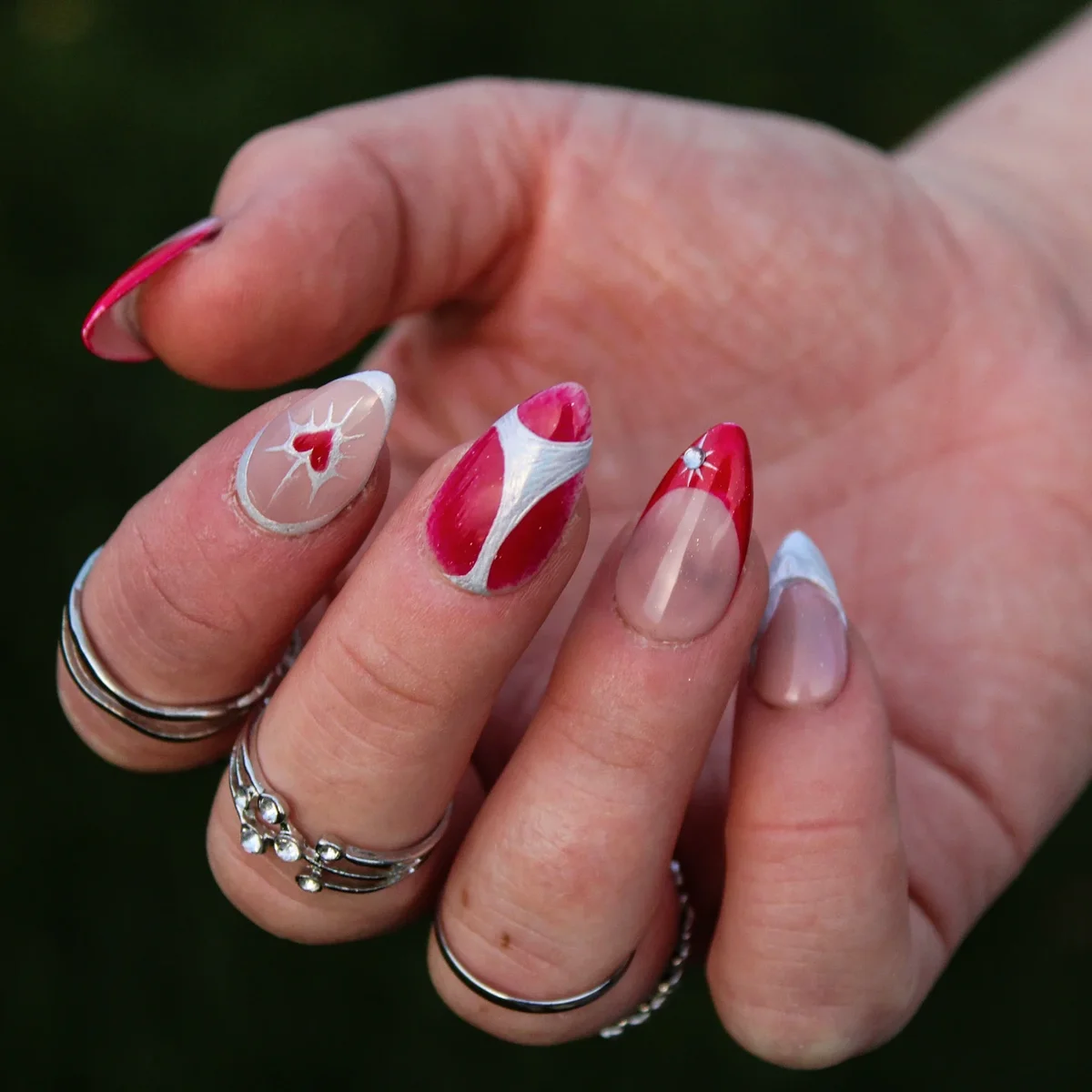 Nude almond nails with red and white curved tips, hearts and small star accents.