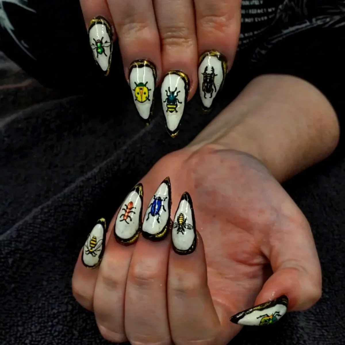 Pale pointed nails with dark outlines and colourful insect illustrations.