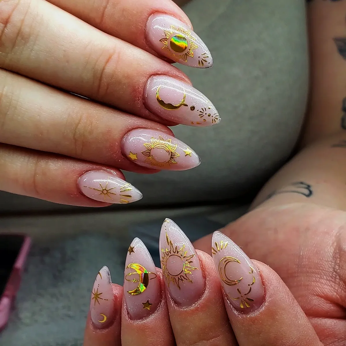 Nude pointed nails with fine gold suns, moons and stars.