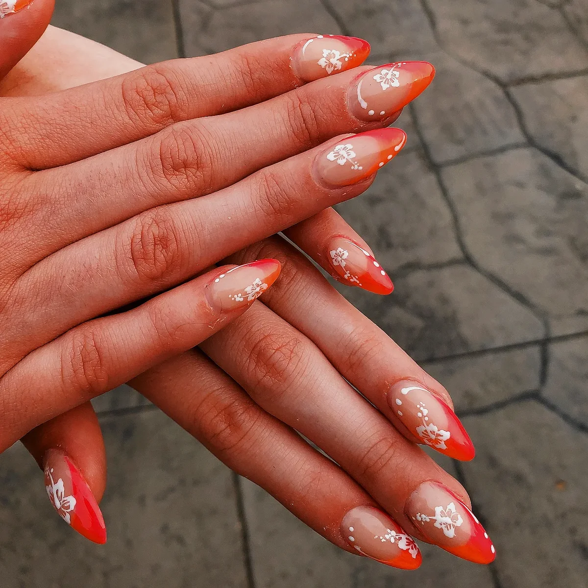 Nude almond nails with bright orange tips and small white flowers.